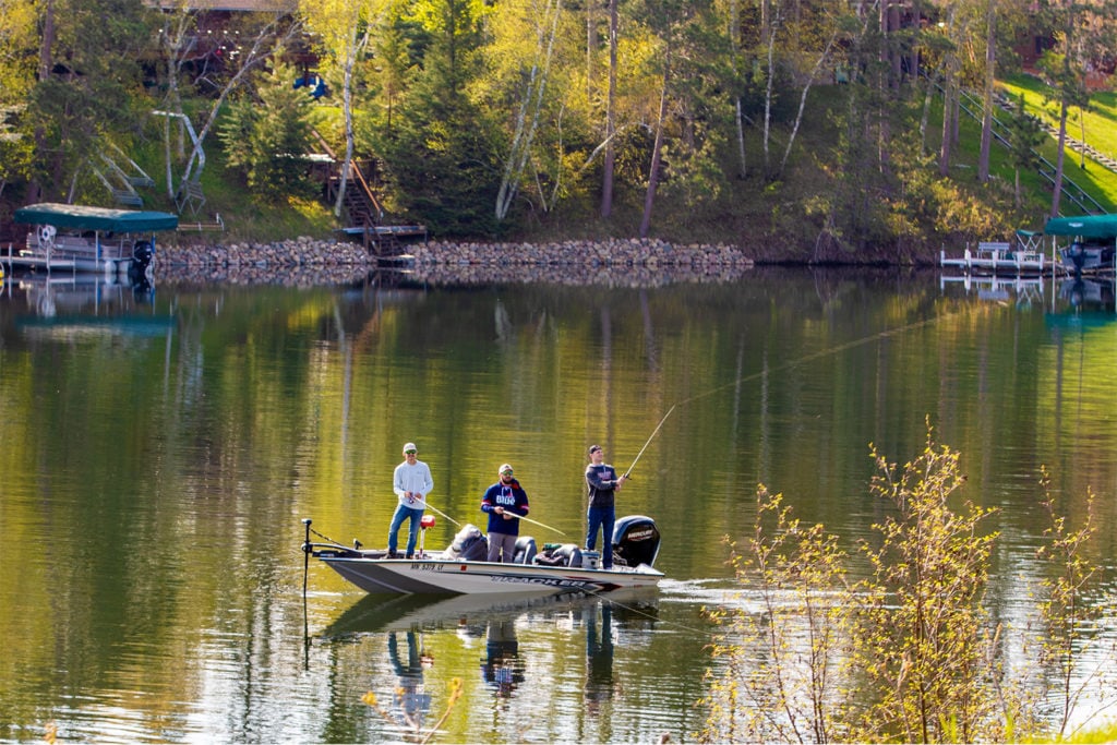 Three men fishing off of a boat on a lake