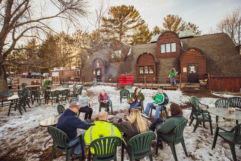 lodge and people eating outside in winter around fires