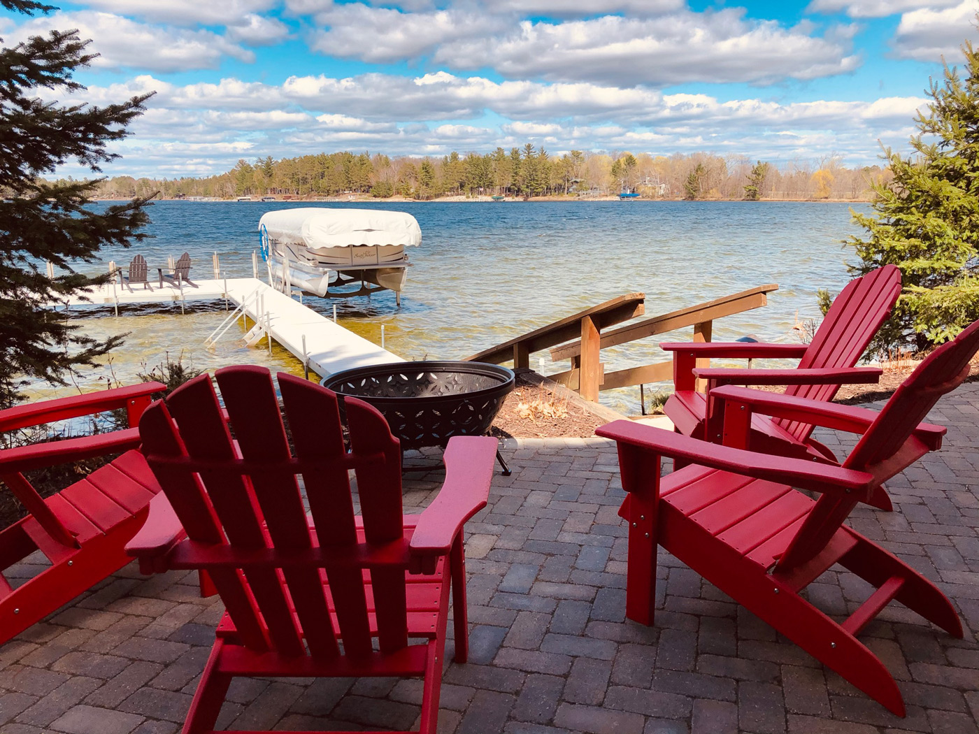 Adirondack chairs around fire pit overlooking a dock on a lake