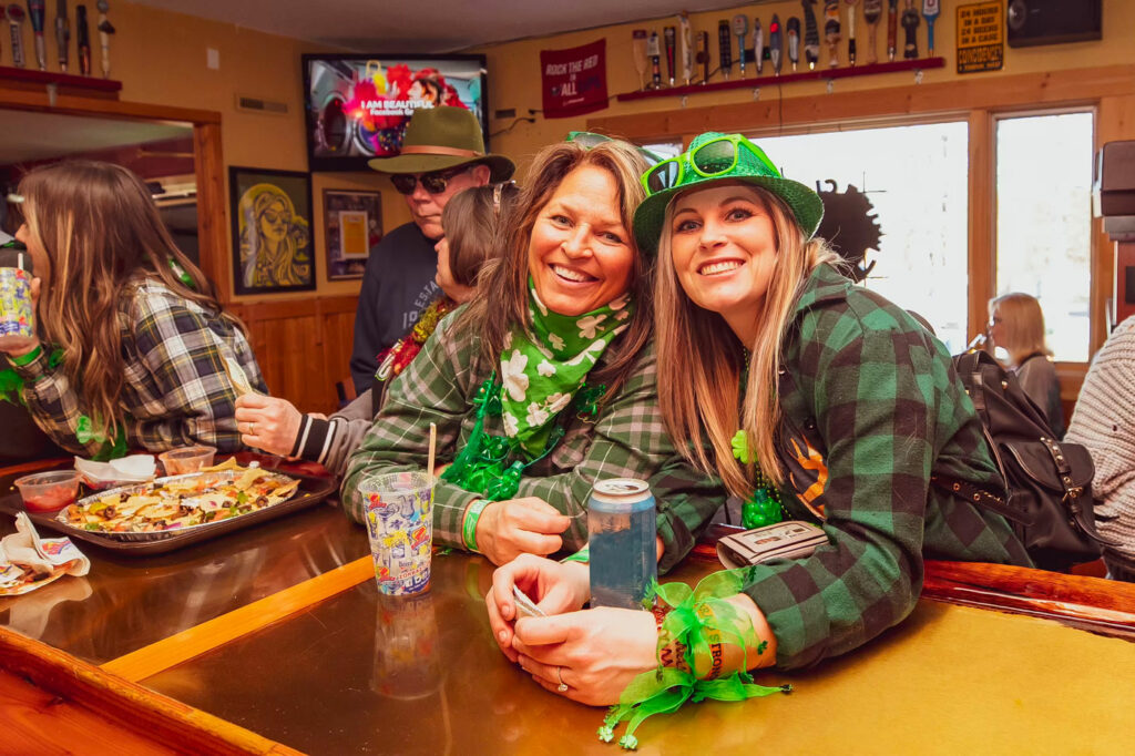 Two women wearing St. Patrick's Day outfits drinking at the bar.